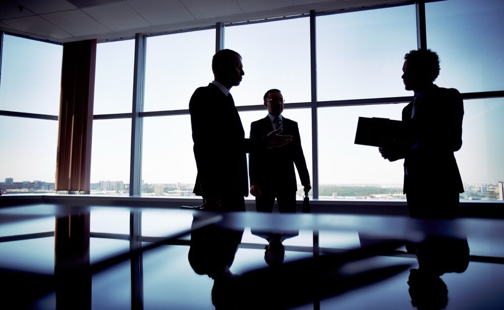 Business leaders in conversation silhouetted against office windows