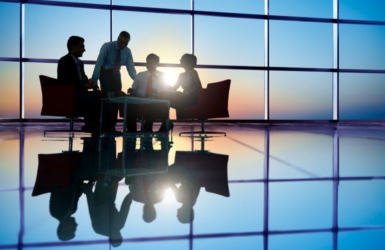 Executive team working at sunset in glass boardroom